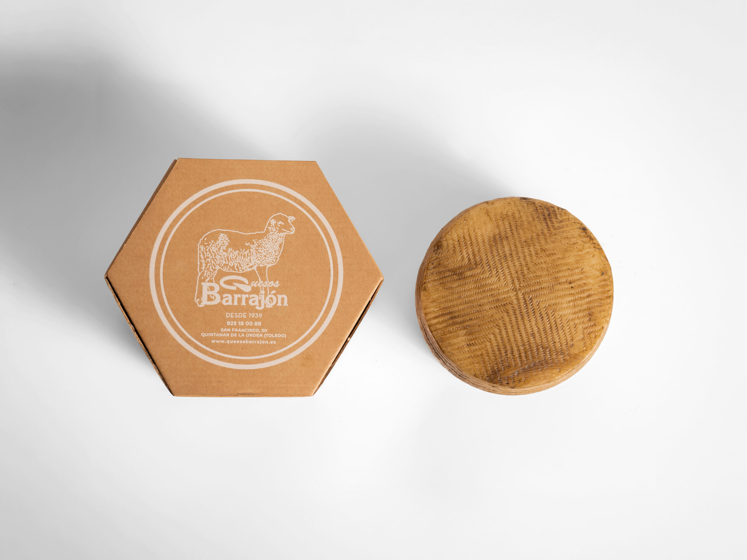 Caja de regalo hexagonal de Quesos Barrajón junto a una rueda de queso
